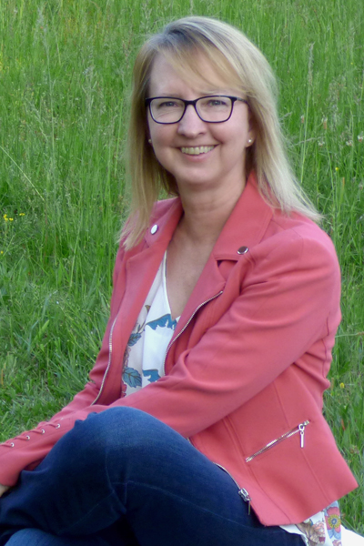 Jackie smiling at camera sitting on a white leather footstool with a green pasture as the background